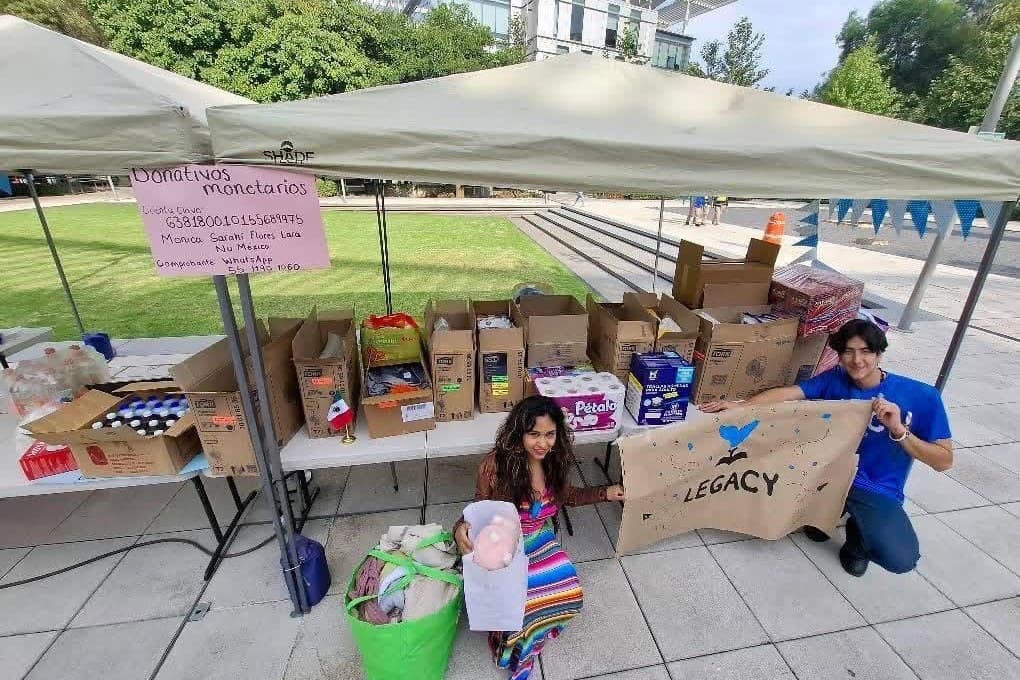 Colecta de donativos: mesas con cajas, despensas y la lona de LEGACY